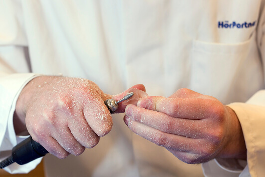 Ein Hörakustiker fertigt ein individuelles Hörgerät in präziser Handarbeit an.